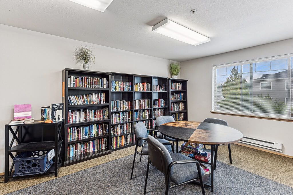 A room with a large bookshelf filled with books, a small table, and chairs.